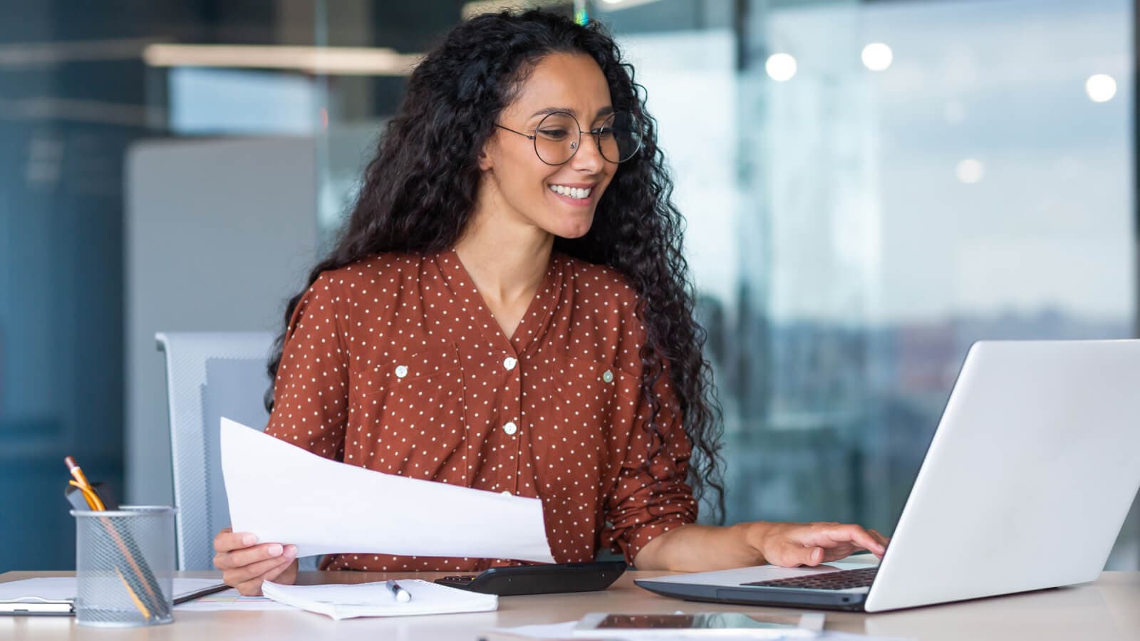 Woman in spotty brown blouse grinning at laptop