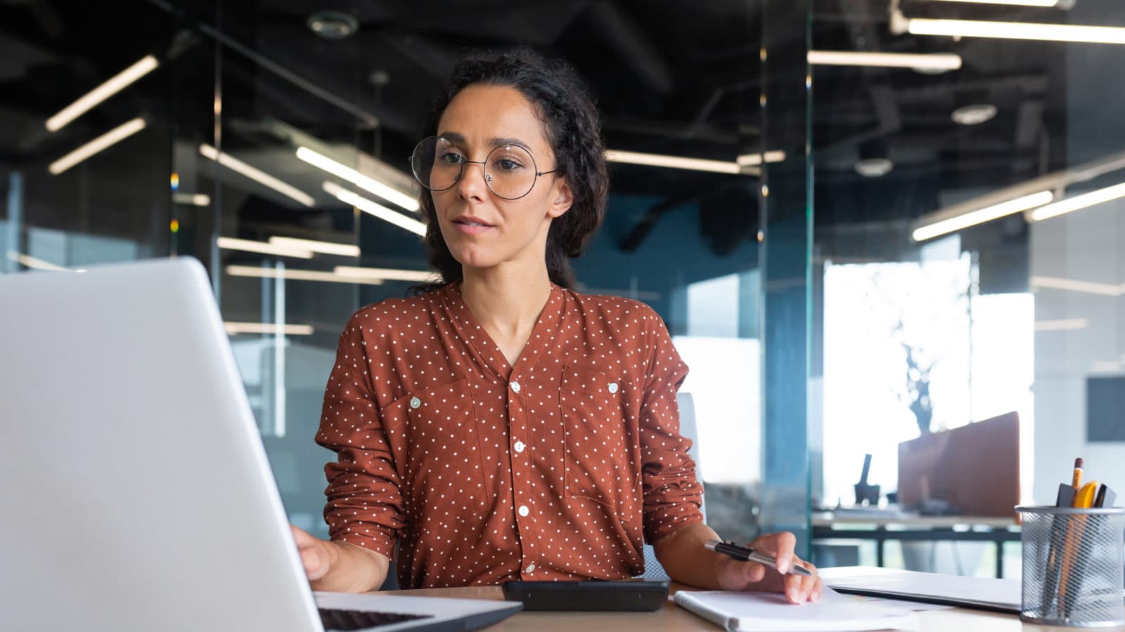 Woman looking at laptop screen and holding pen