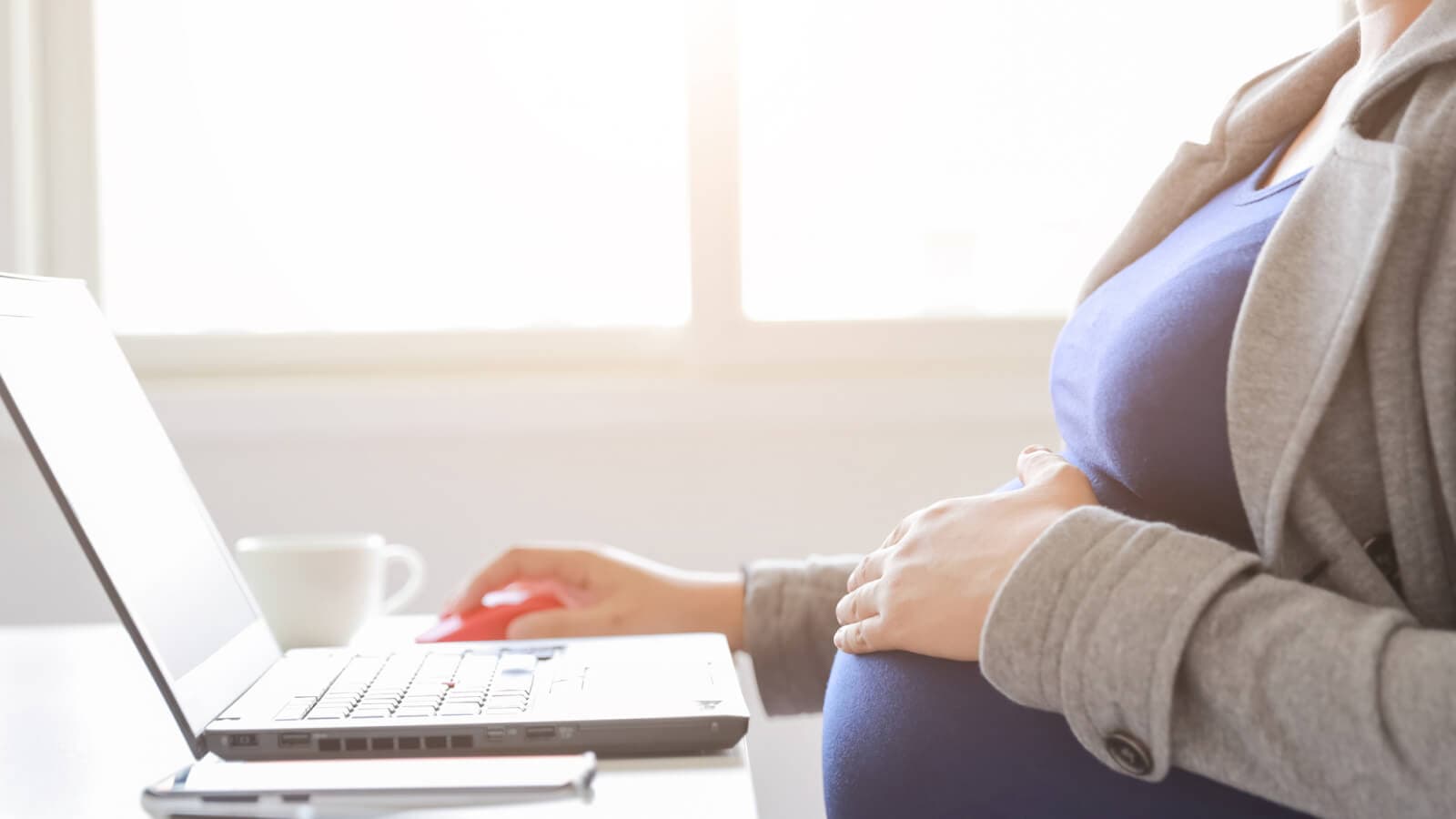 Baby bump with hand on in front of laptop