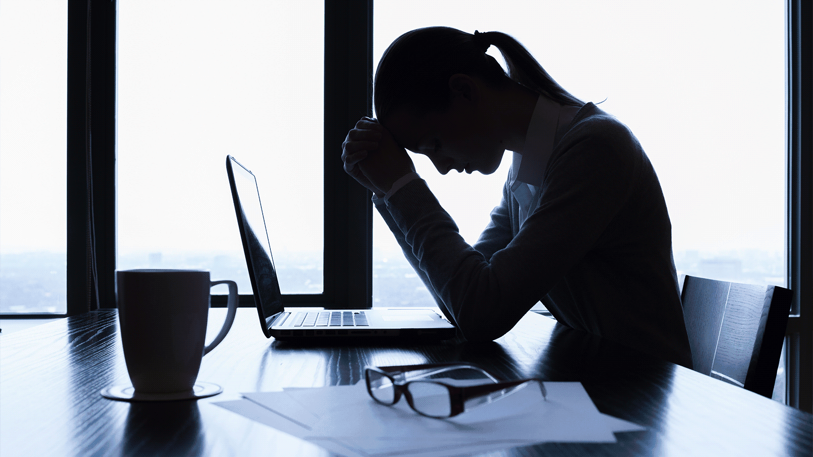 Silhouette of person with head in hands at desk