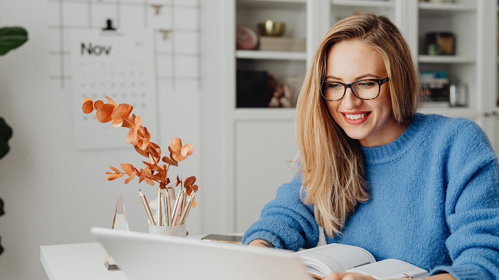 Woman in blue jumper smiling at laptop