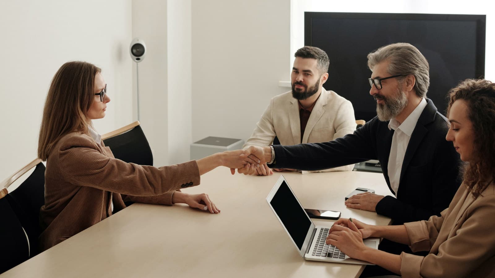 Four people round a table, two shaking hands