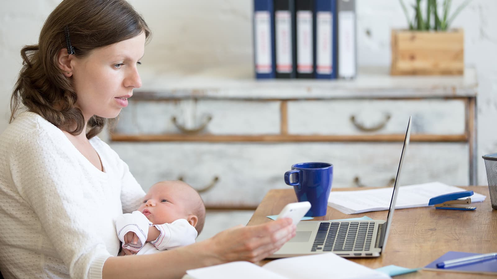Woman working on a laptop while holding her baby