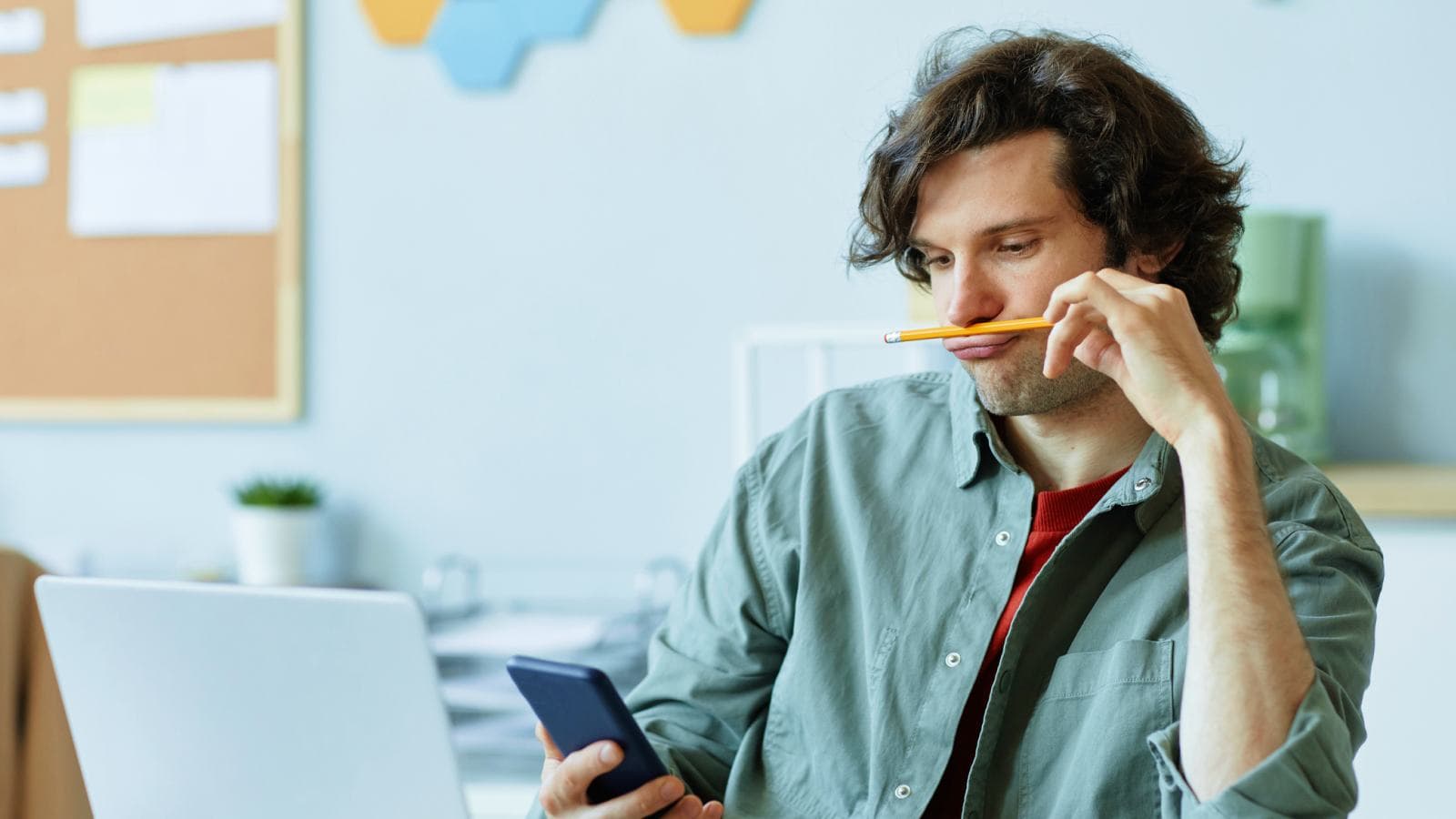 Man looking at phone, holding pencil under nose