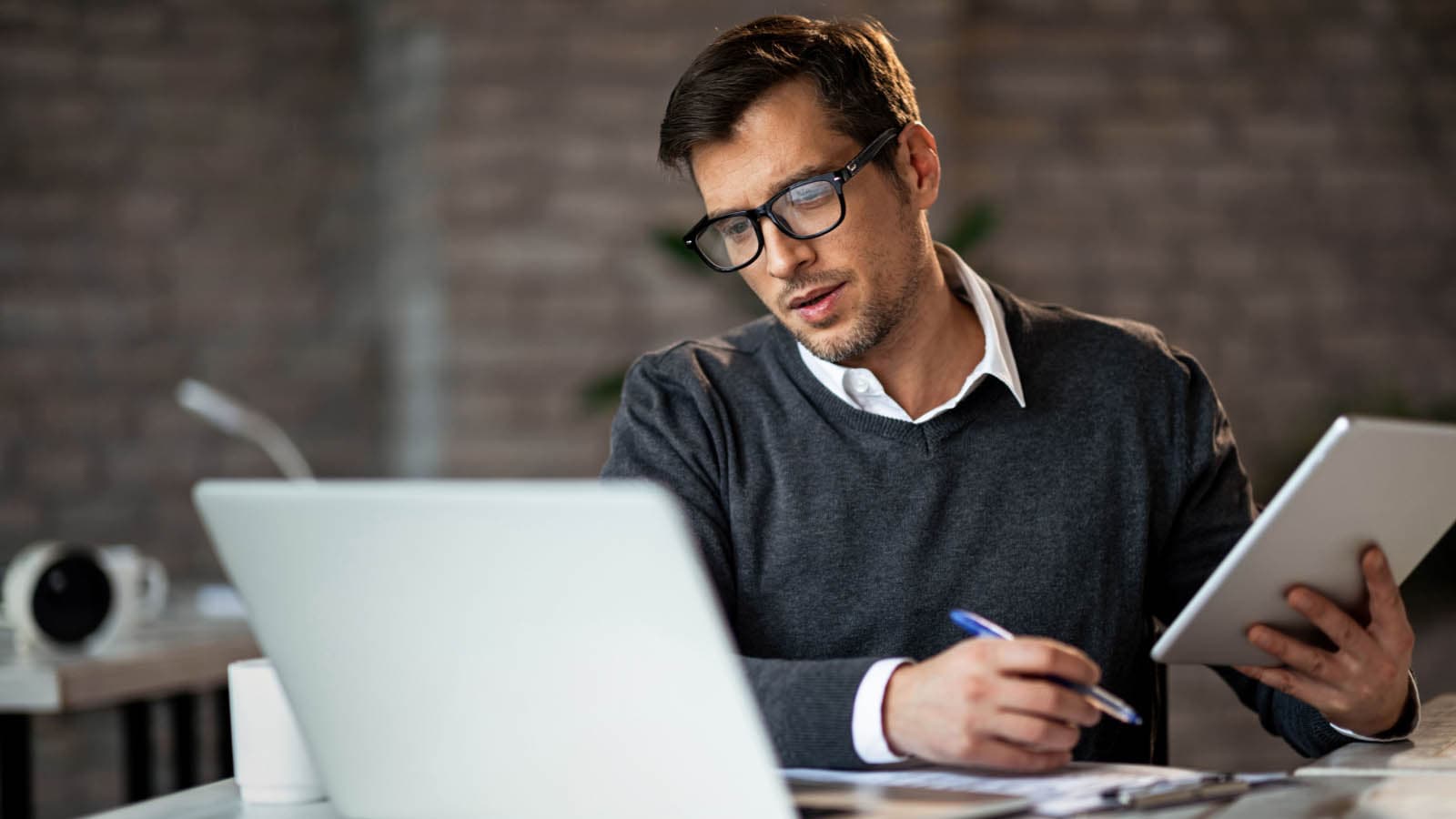 Man holding tablet and pen while looking at laptop