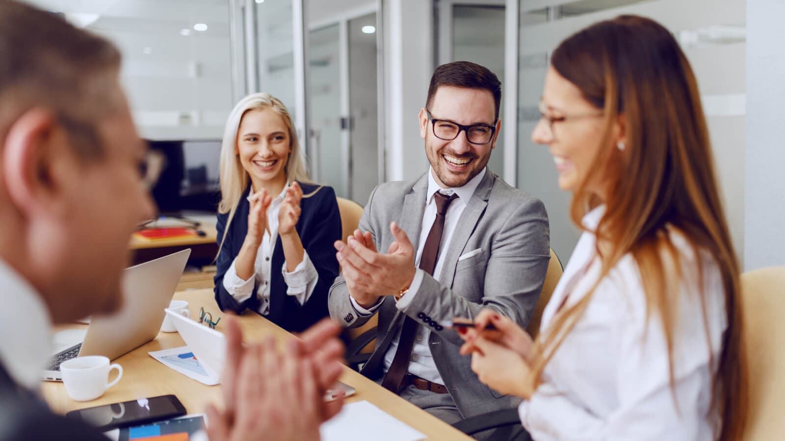 Three people around table applauding woman