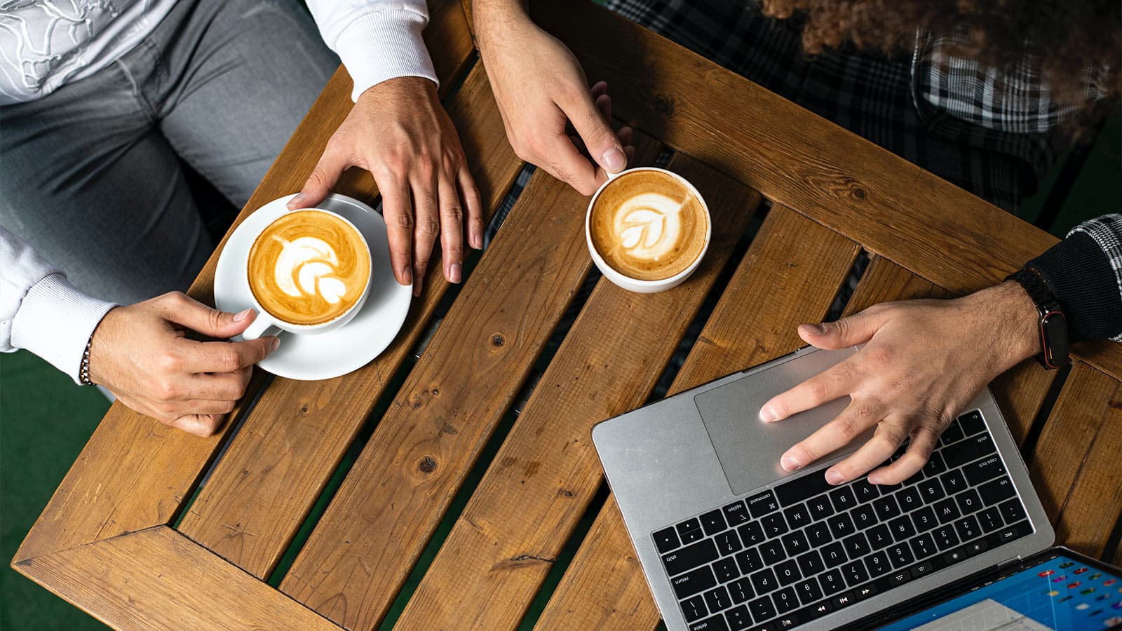 Two people with cappuccinos and a laptop at table
