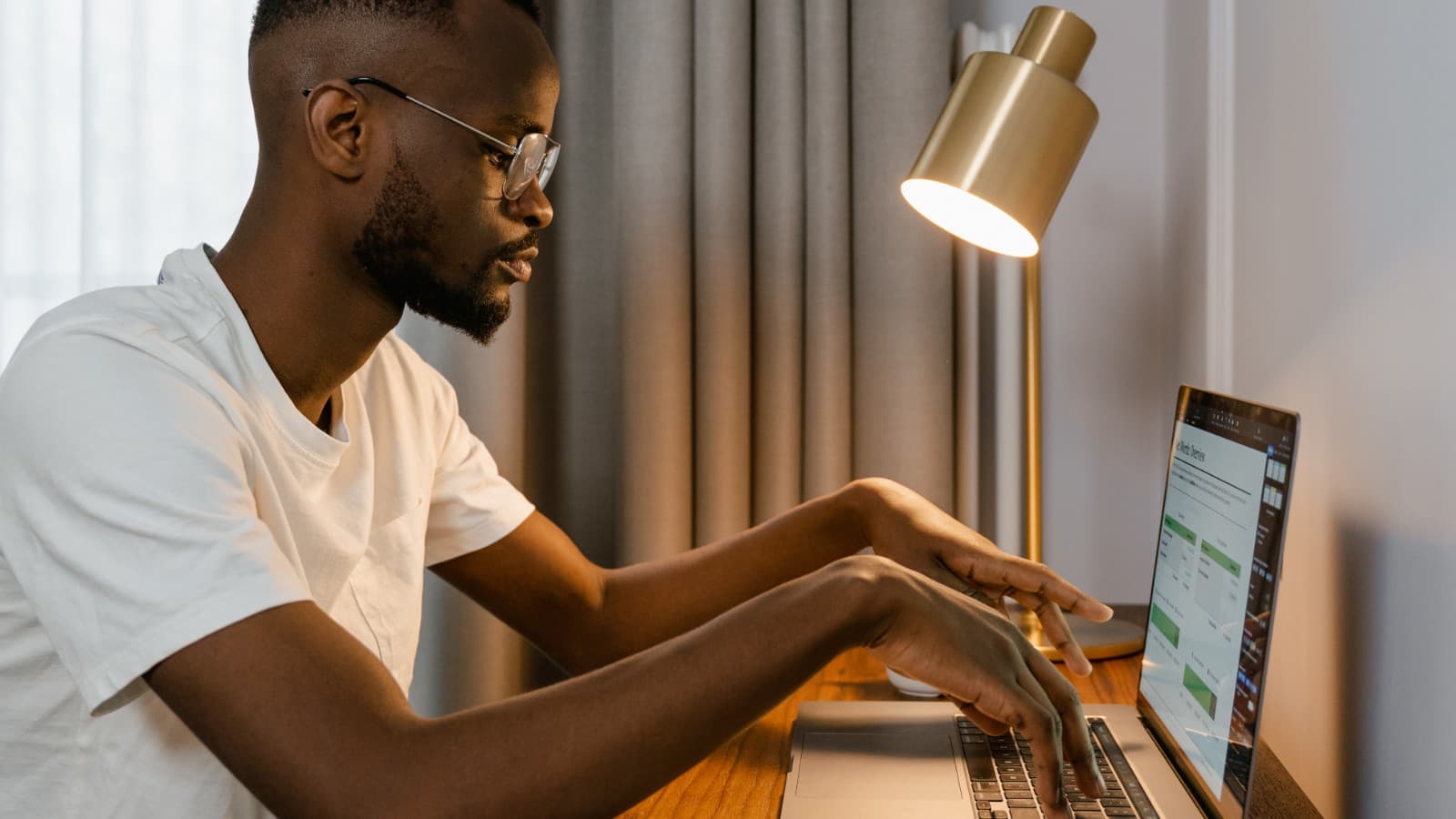 Man typing at laptop on desk with lamp