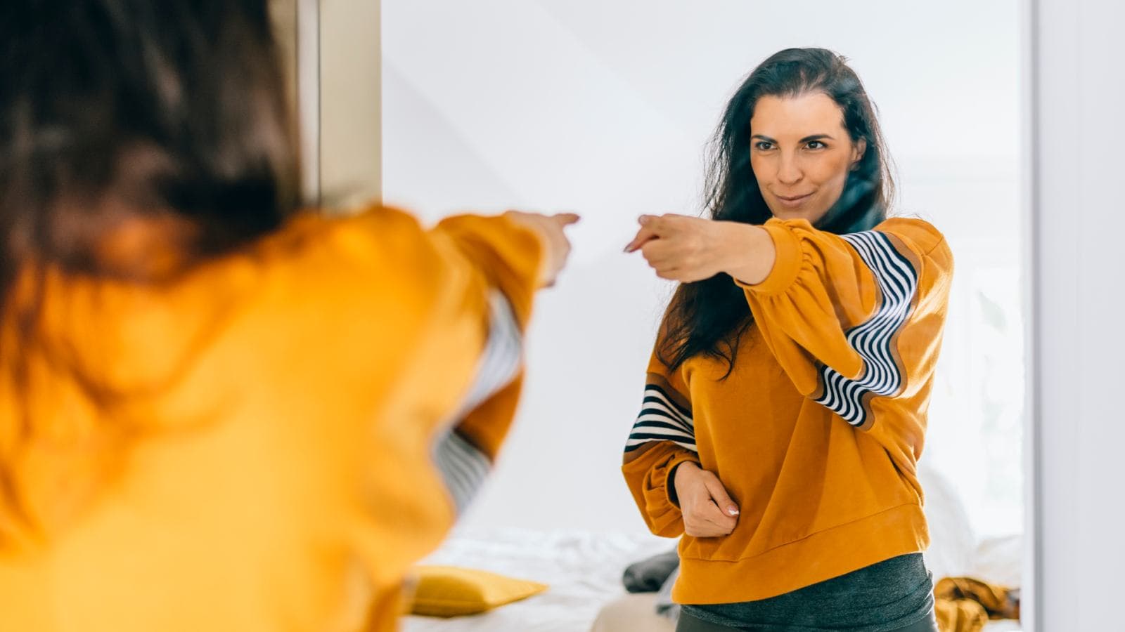 Woman in yellow jumper pointing at mirror
