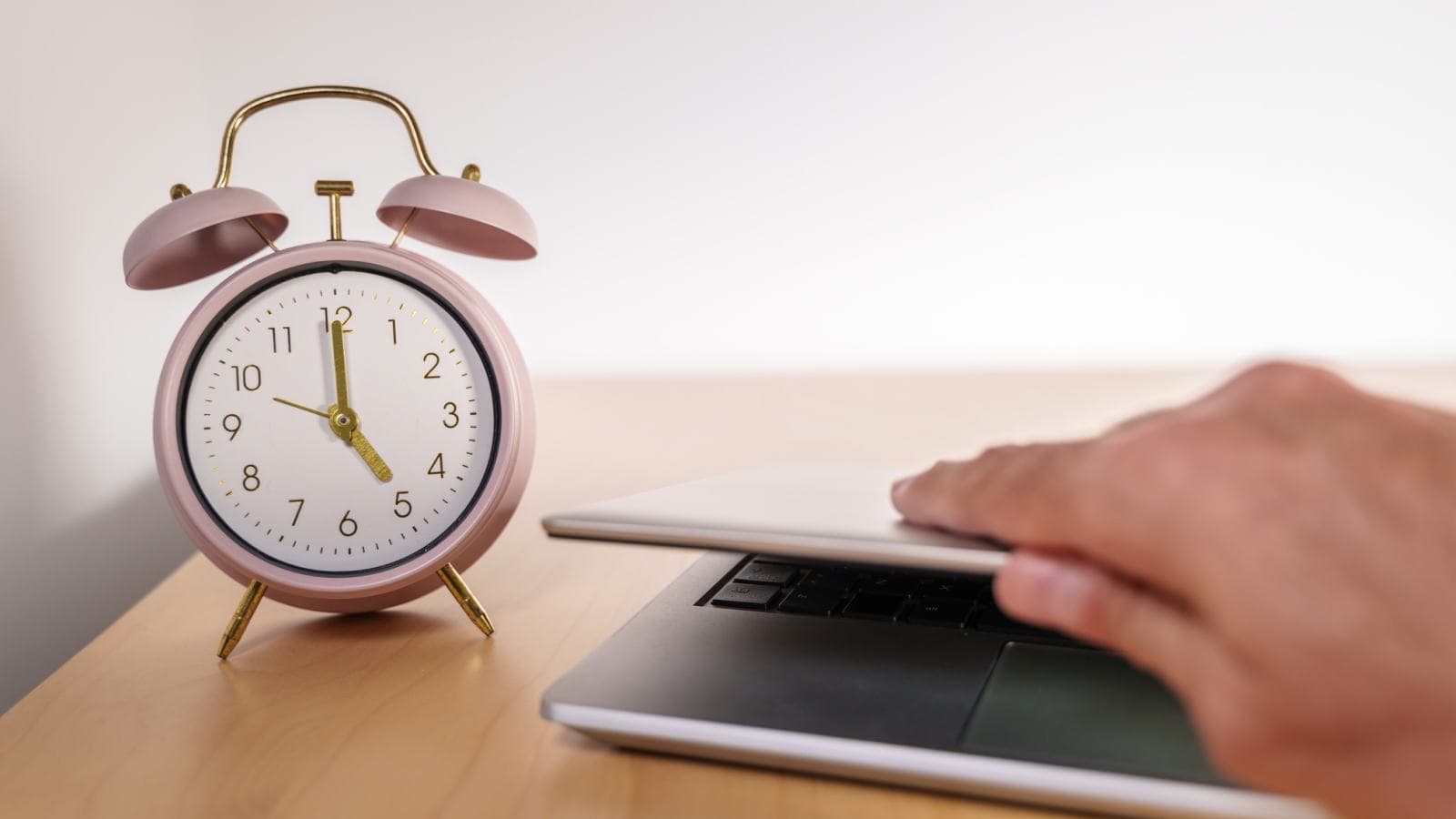 Pink alarm clock and hand opening a laptop