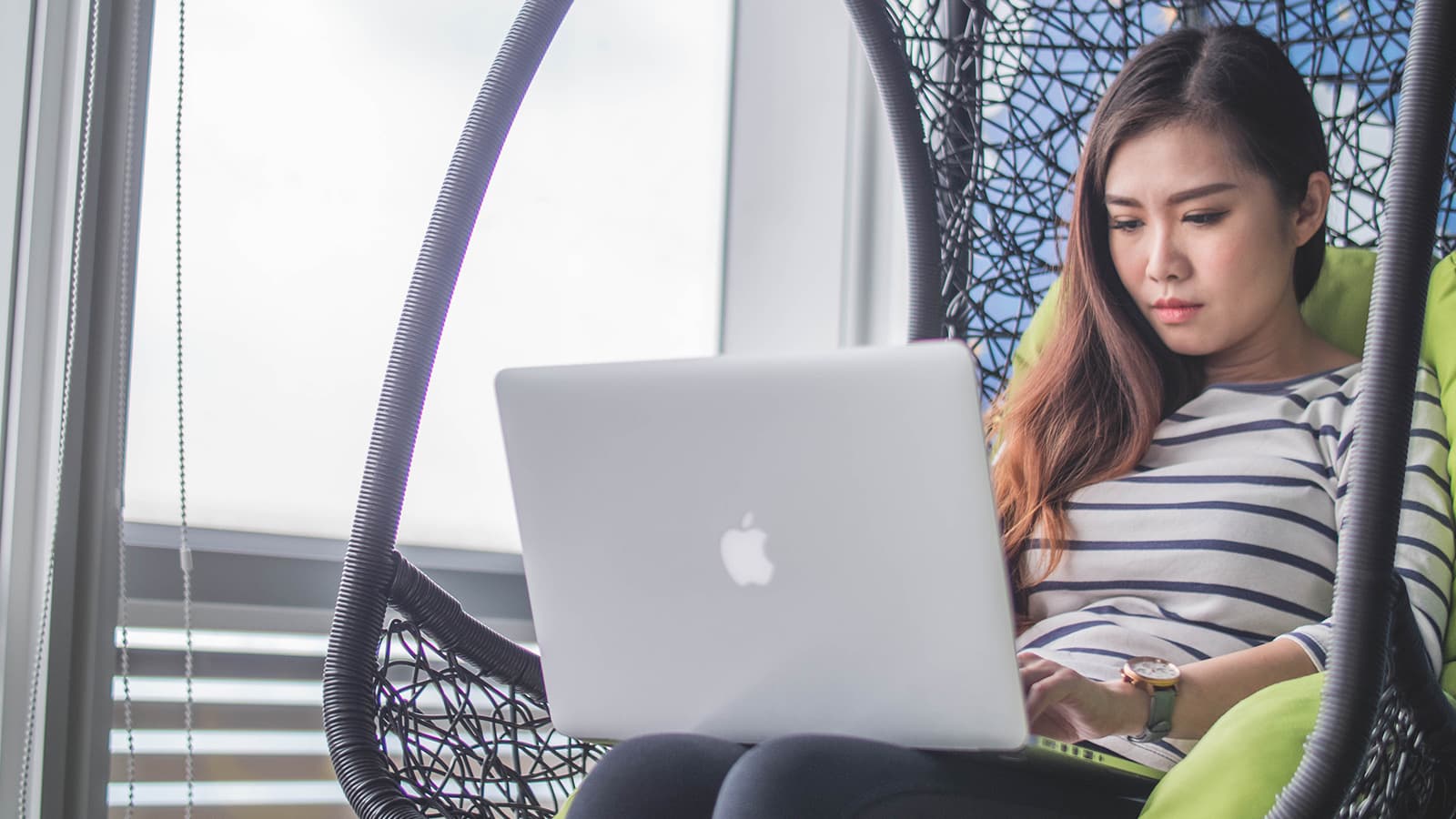 Woman using laptop in hanging nest chair