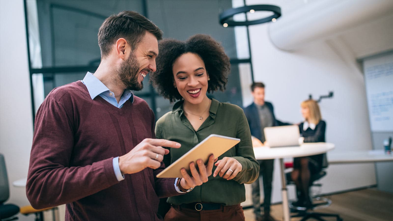 Two people standing in office, smiling at tablet