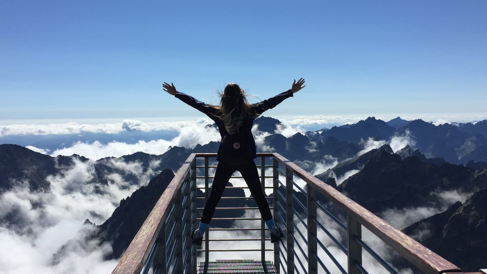 Man with arms out, above clouds and mountains